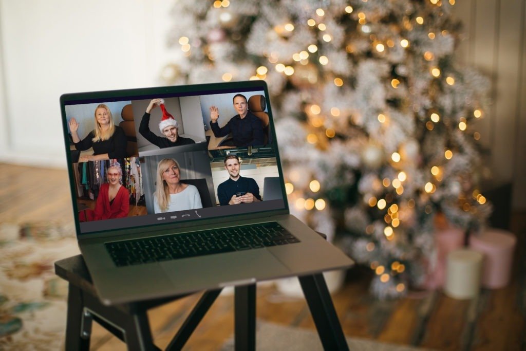 Photo of a laptop with lit tree in the background and a Zoom meeting of 4 other people wearing Santa hats and other festive wear.