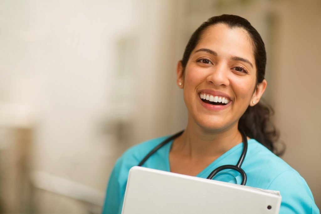 Portrait of a smiling young Hispanic woman in scrubs wearing a stethoscope around her neck