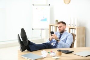 Lazy office employee with mobile phone at workplace