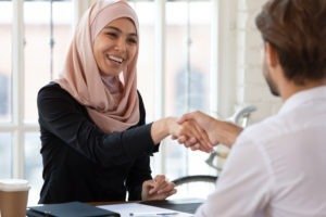 Smiling Asian Muslim hijabi businesswoman shaking white male businessman's hand