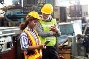 Professional Mechanical Engineer team of young black woman and older white man discussing something on tablet while wearing safety vests and hard hats